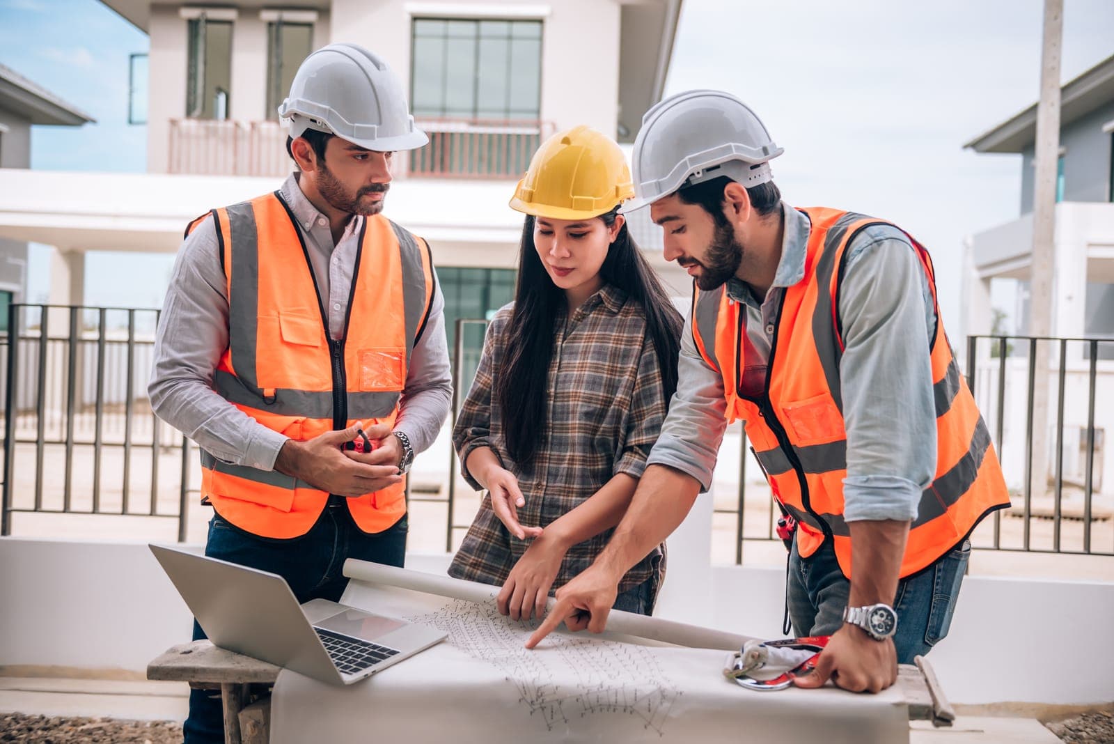 Civil engineer, construction worker and architects in hardhats and safety vests collaborating on a building site